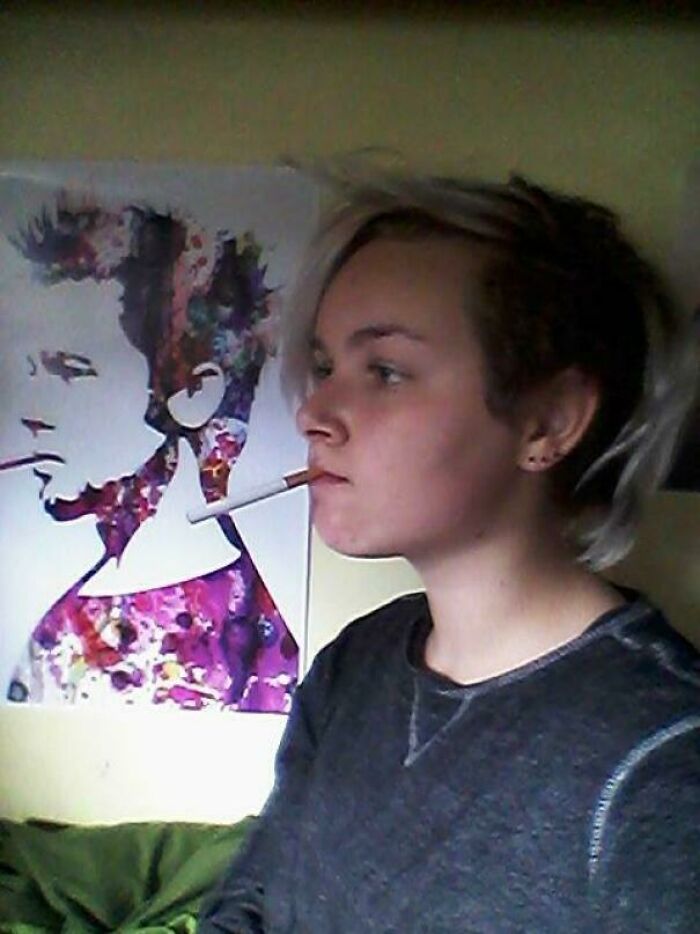 Young person smoking indoors with a cigarette, sitting by colorful wall art, reflecting on their regrettable past moments.