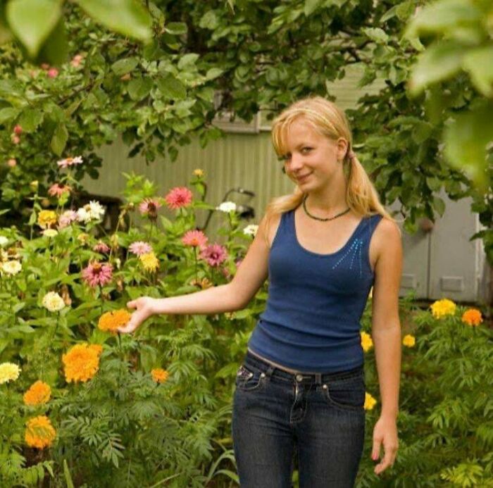 Young woman in casual blue top and jeans posing in a colorful garden, evoking a relatable regrettable past moment.