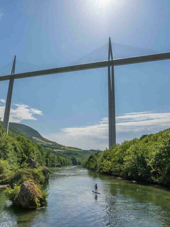 Massive cable-stayed bridge towering over a river with a person paddleboarding below showing scale of megalophobia