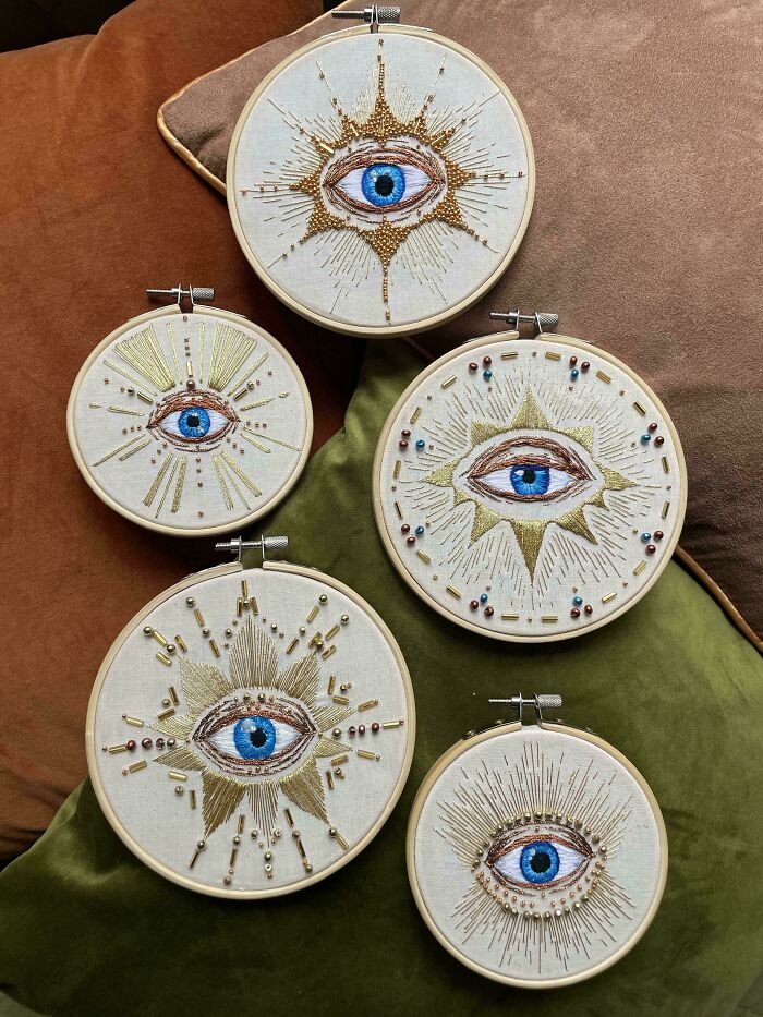 Five embroidery hoops displaying intricate and beautiful embroidery skills featuring blue eyes and golden designs.
