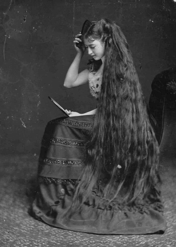 Vintage black and white photo of a woman with extremely long hair reading, a candid glimpse into the past.