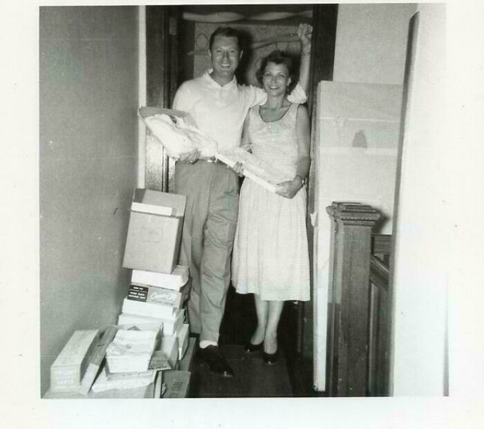Black and white candid vintage photo of a smiling couple posing inside a hallway with stacked boxes, history glimpse