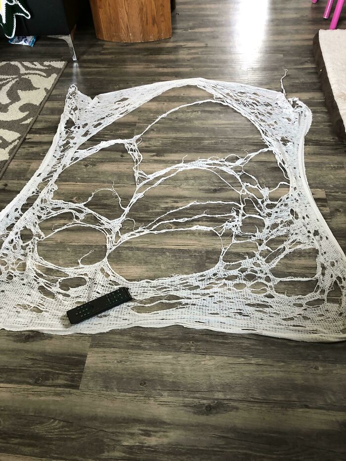 Worn-out white netting on a wooden floor with a remote control, showing effects of things used over time.