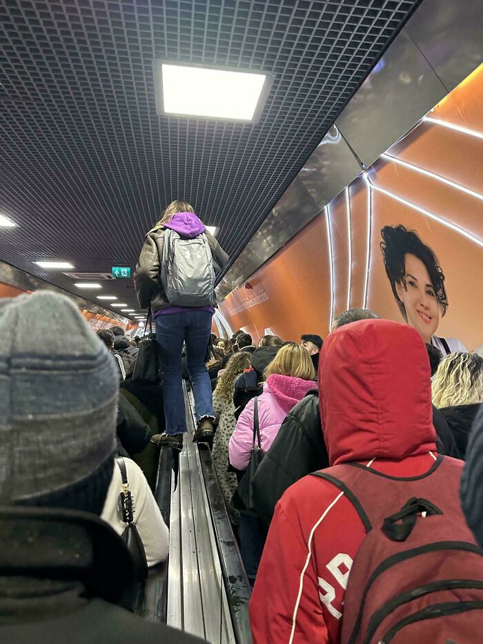 Person walking on a crowded escalator railing, showing entitled behavior in a busy subway station.