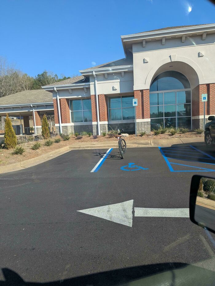 Bicycle parked in a disabled spot in front of a building, highlighting entitled behavior.