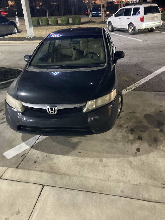 Poor parking job by an entitled person, black car parked awkwardly over lines in a parking lot at night.