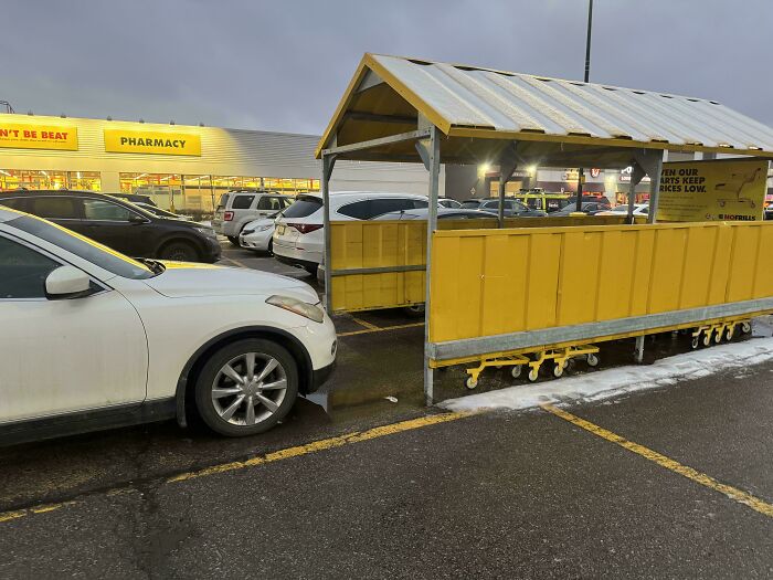 A car parked blocking a yellow cart return at a shopping plaza, illustrating entitled behavior.