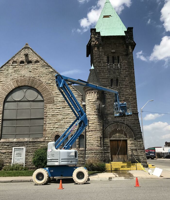 Crane lift by historic building tower, illustrating time's impact on things.