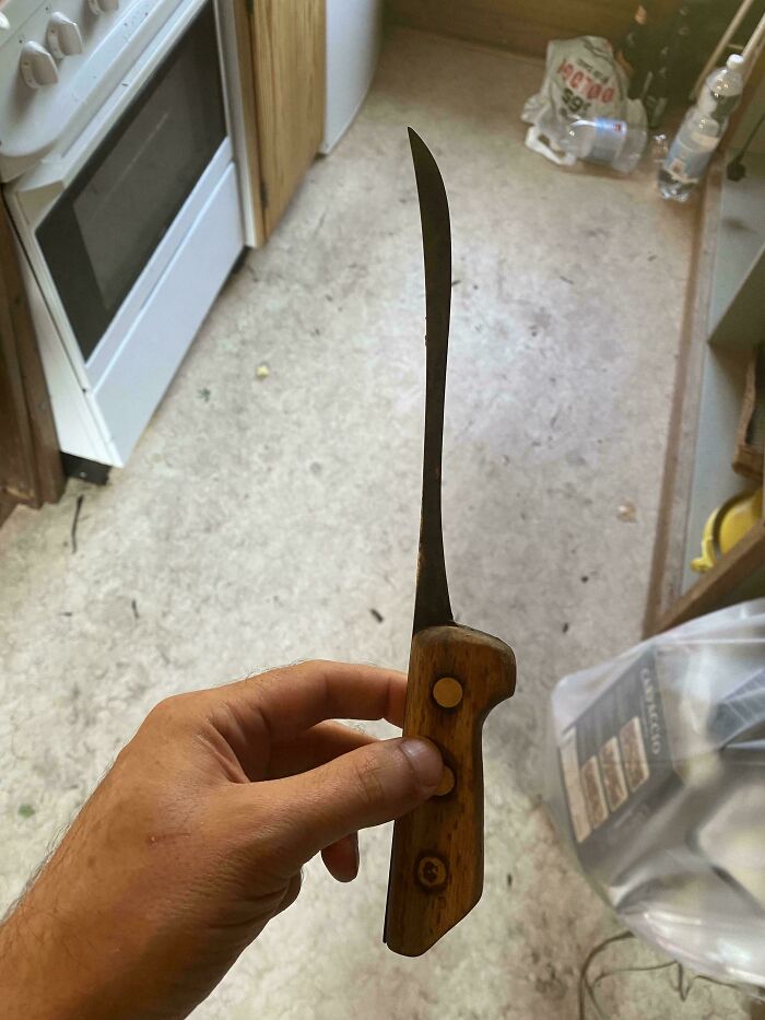 Hand holding a uniquely shaped knife with a wooden handle, illustrating intriguing things in a kitchen setting.
