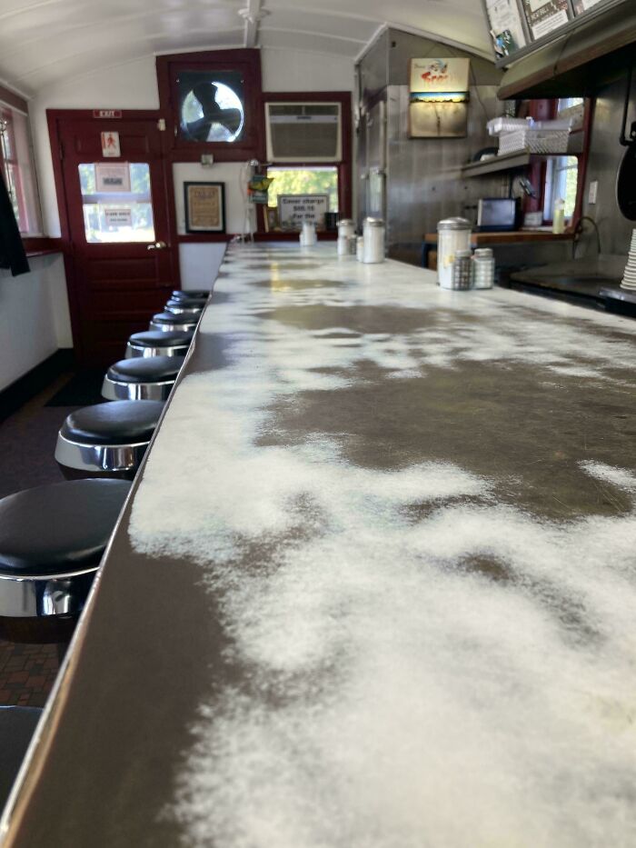Diner counter covered in flour with empty stools and retro kitchen, highlighting time vs. things.