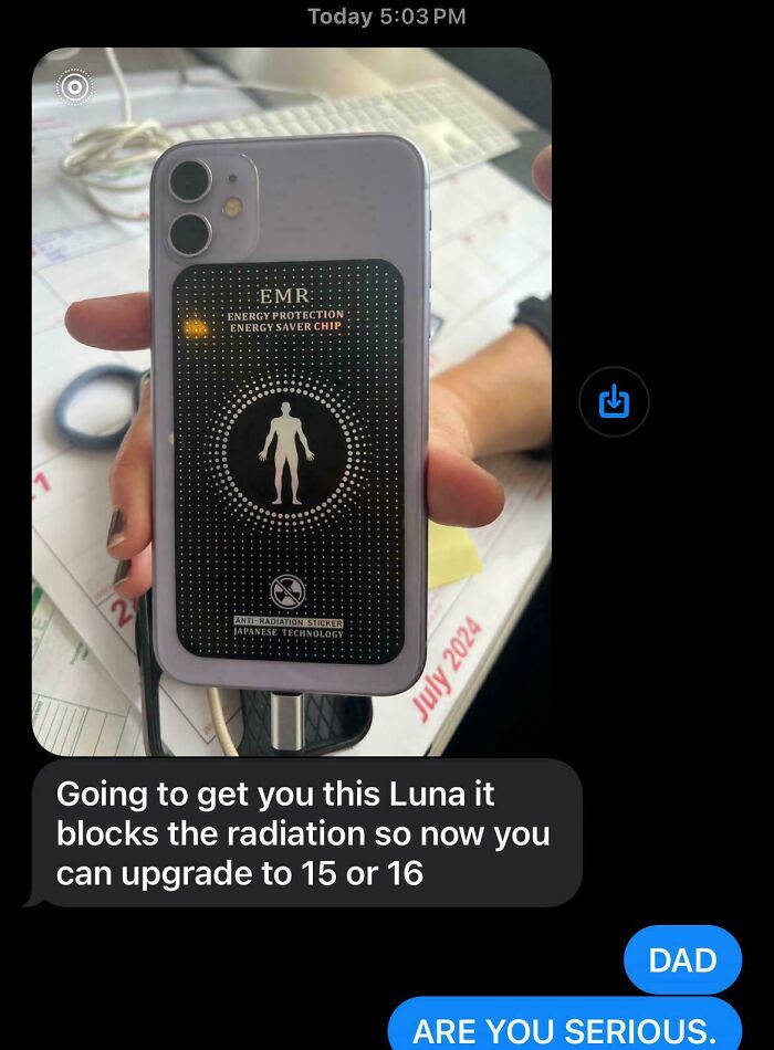 Smartphone with an anti-radiation sticker scam, held over a desk with calendar in background.