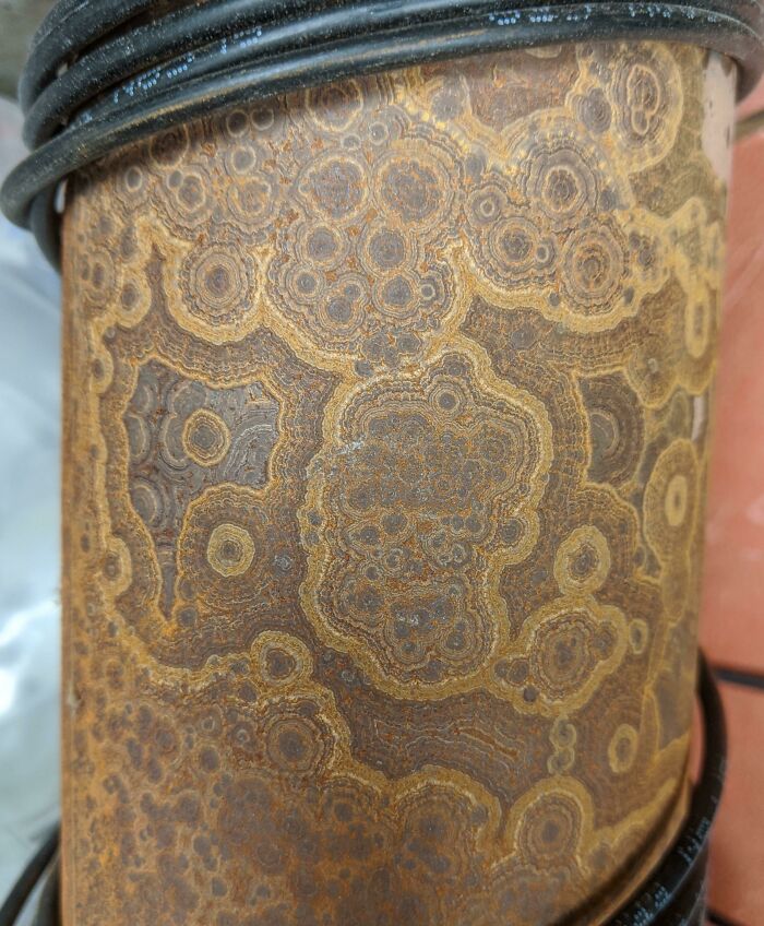 Close-up of a rusty metal pipe with intricate circular patterns, showcasing the effects of time on things.