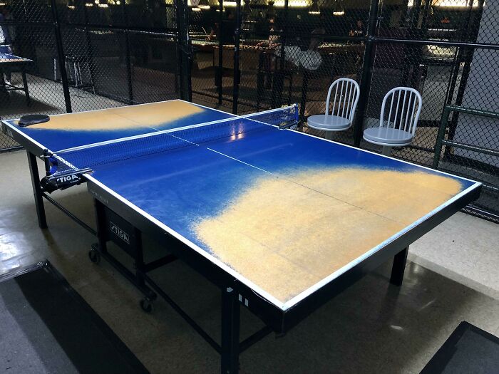Ping pong table with faded paint showing signs of time, two chairs in the background.