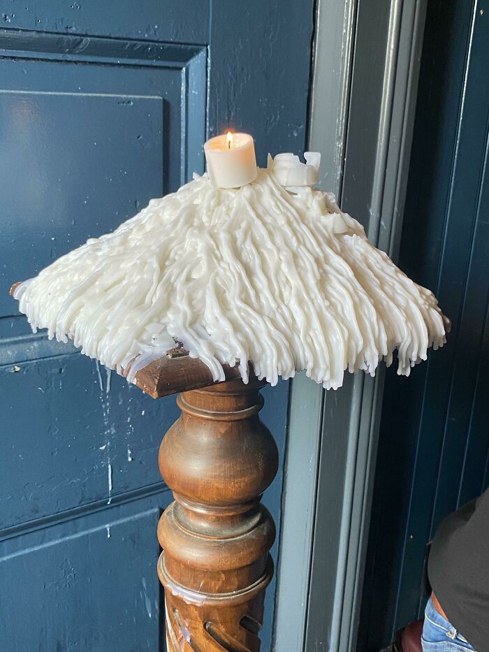 Candle wax dripped over time, forming intricate layers on a wooden stand next to a blue wall.