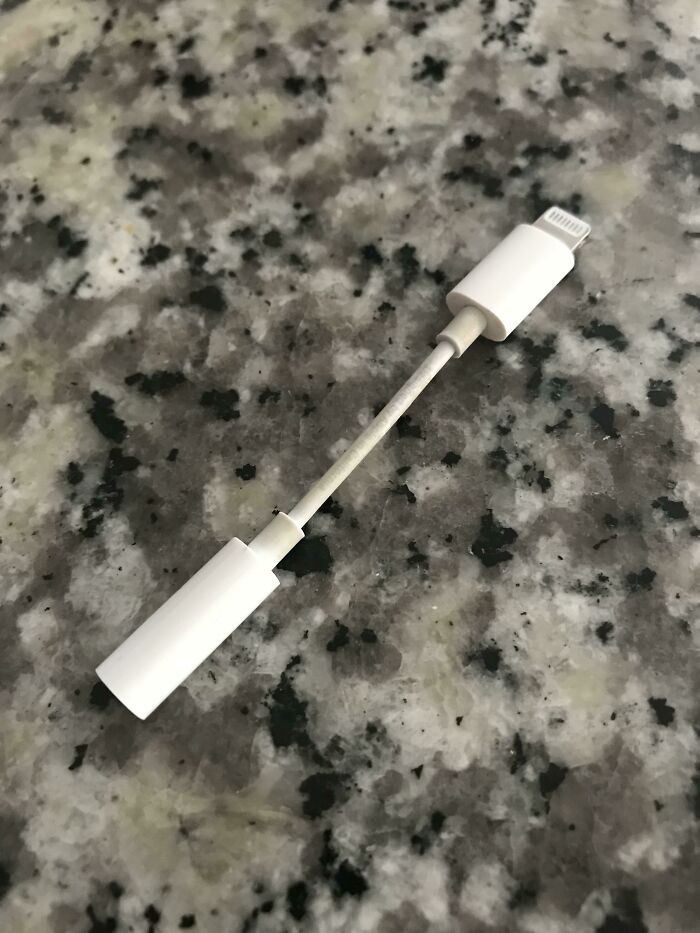 A white headphone adapter on a gray marble surface, associated with shameless scams.
