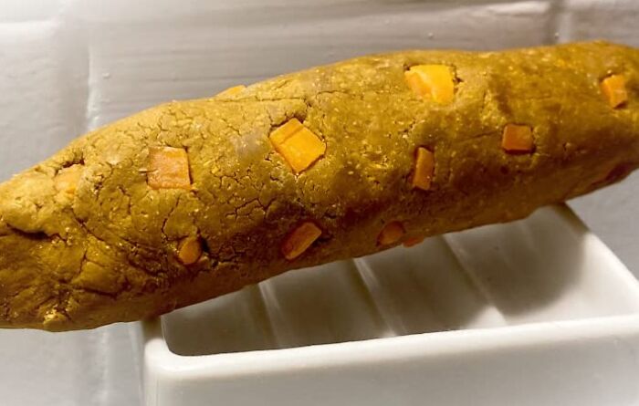 A humorous, realistic-looking fake p**p with orange bits, highlighting toilet humour on a soap dish in a bathroom setting.