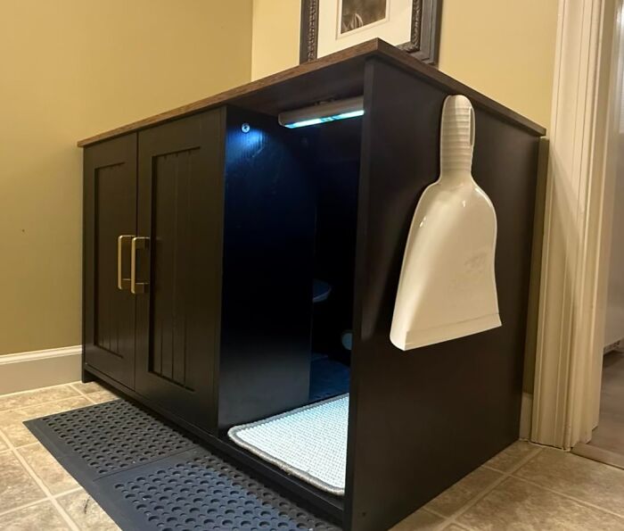 Black wooden storage cabinet with LED light and dustpan attached, illustrating sneakily useful decor items that earn their keep.