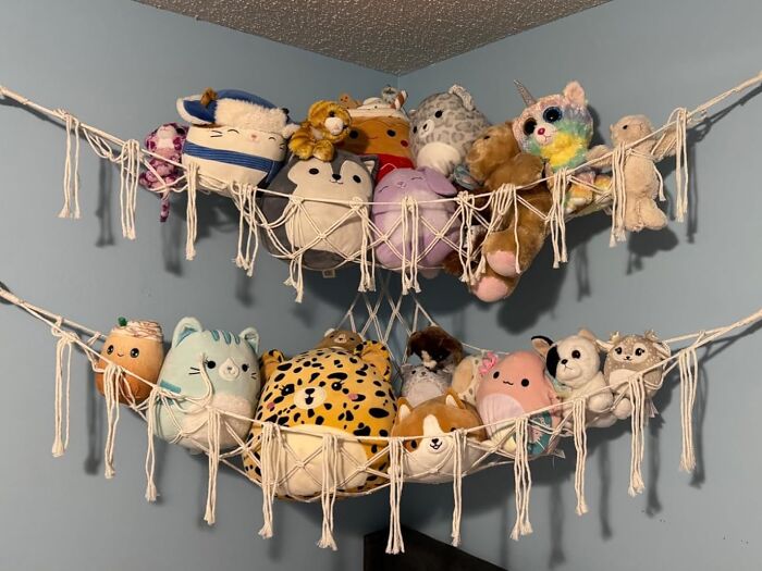 Stuffed animals displayed in a quirky, functional rope hammock on a blue wall.