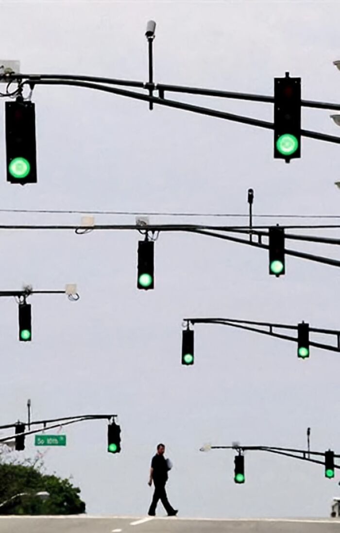 A person walks under an array of green traffic lights, creating a funny scene without context.
