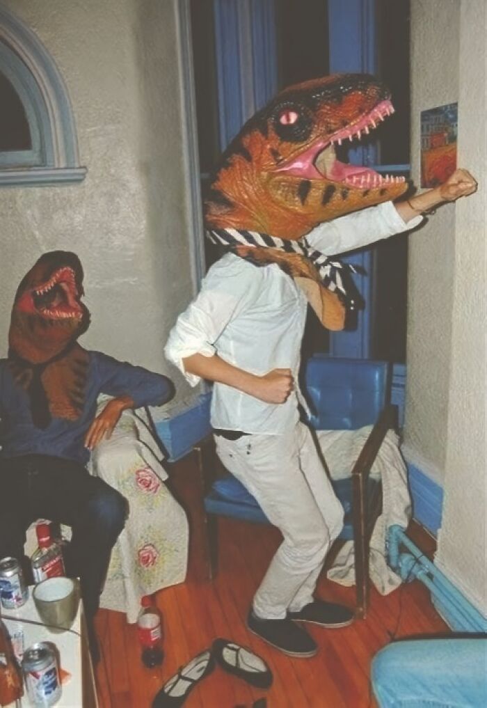 Two people wearing dinosaur masks indoors, one posing humorously.