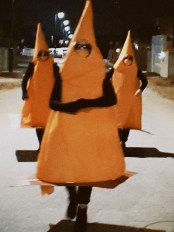 Three people dressed as traffic cones walking down a street at night, adding humor without context.