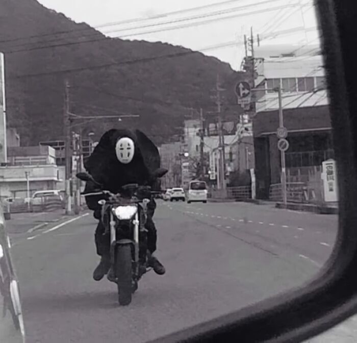 Person in a mysterious costume riding a motorcycle on a city street, captured in a funny, context-free moment.