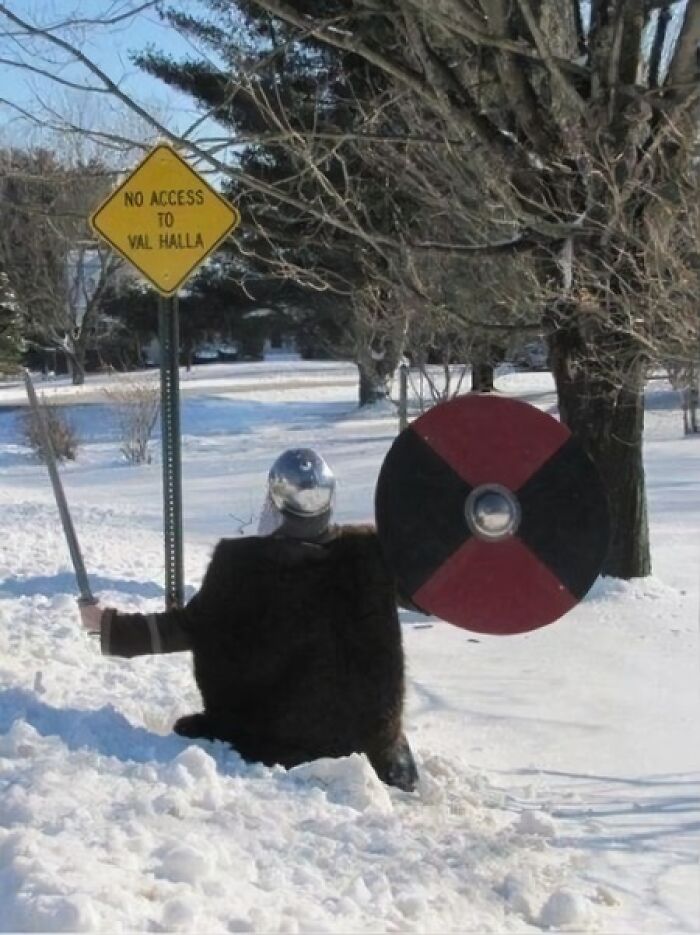 Viking in snow with shield near sign reading "No Access to Valhalla," capturing random funny moment.