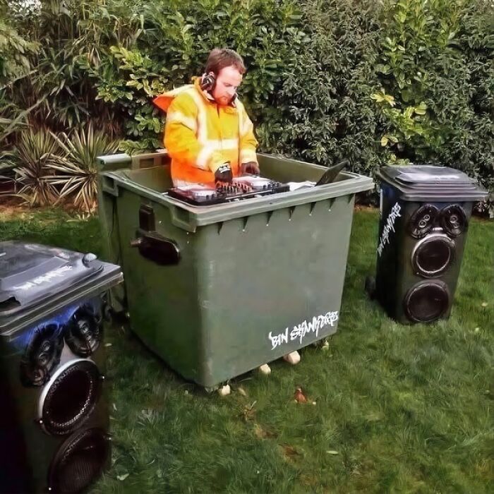 DJ in a funny setting, using a trash bin as a DJ booth, with speakers on trash cans in a garden.
