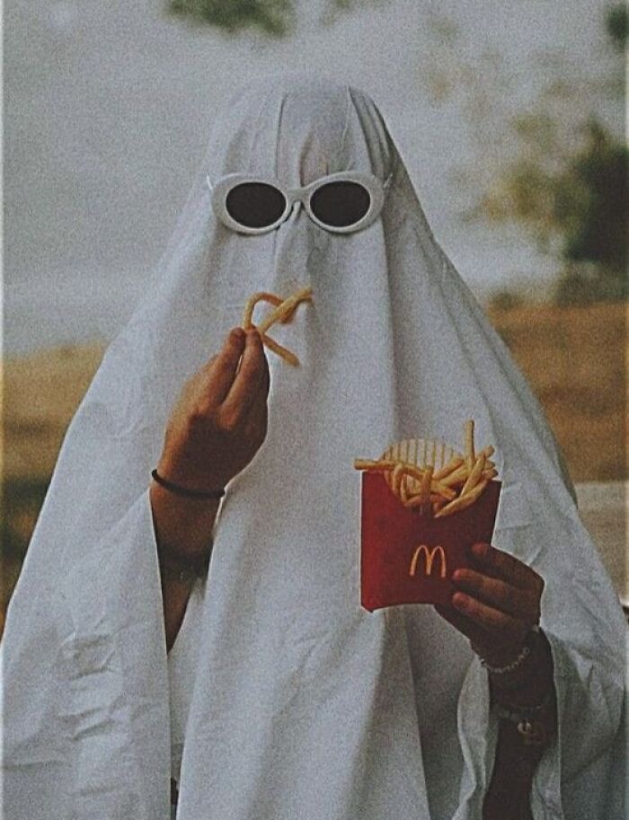 Person in ghost costume wearing sunglasses, holding fries. Funny random photo without context.