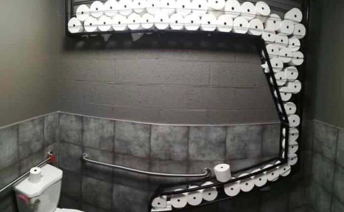 A bathroom with humorous overstock of toilet paper rolls covering the wall.