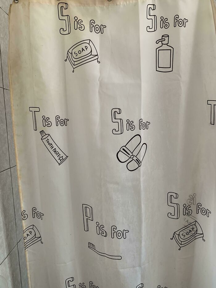 Shower curtain with design fails: mismatched letters and items like soap, toothpaste, slippers, and toothbrush.