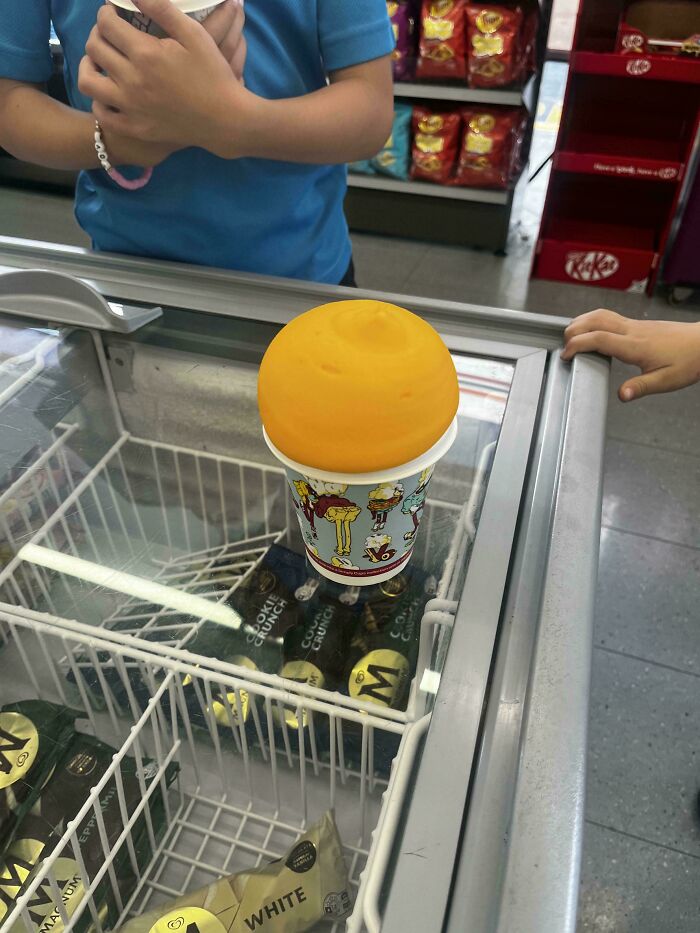 Bright orange ice cream in a cartoon-themed cup at an Australian shop, highlighting quirky local finds.
