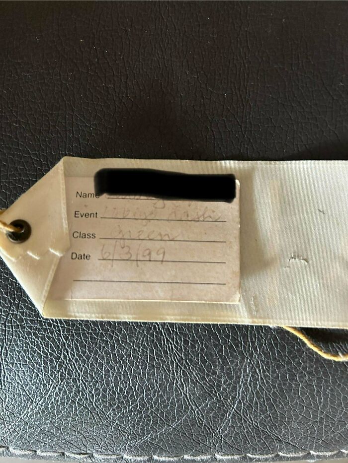 Luggage tag from the 90s with handwritten event, class, and date details on a textured black surface.