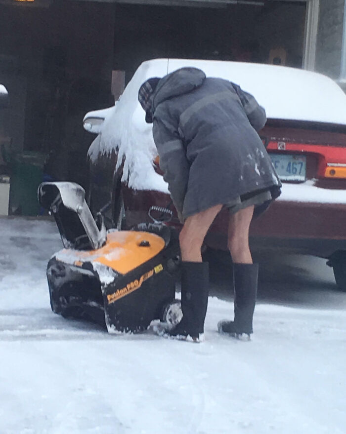 A person in winter attire using a snowblower, showcasing unique weather adaptation in Canada.