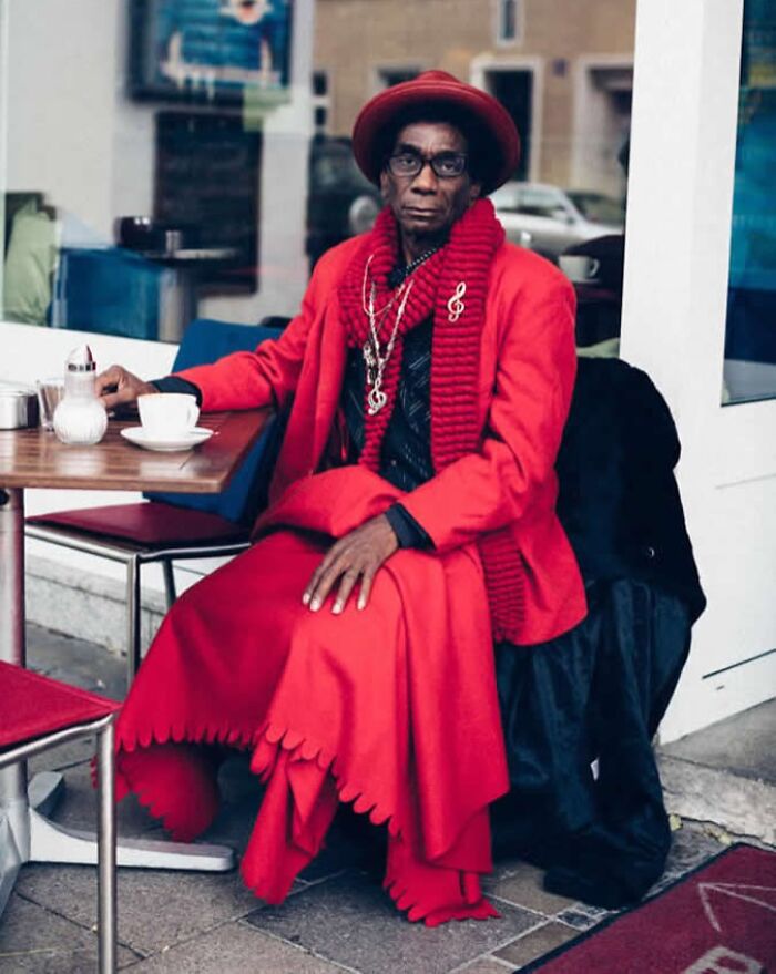 A visually striking street portrait of a stylish stranger in red attire, sitting outside a café with a coffee.