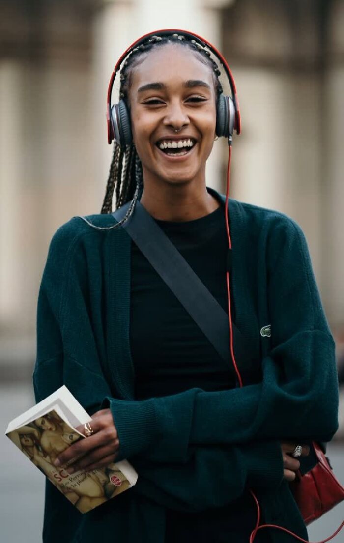 Smiling woman with headphones holds a book, showcasing street portraits' vibrant essence.