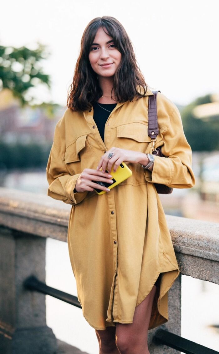 Woman in a yellow dress poses confidently outdoors, captured by a street portrait photographer.