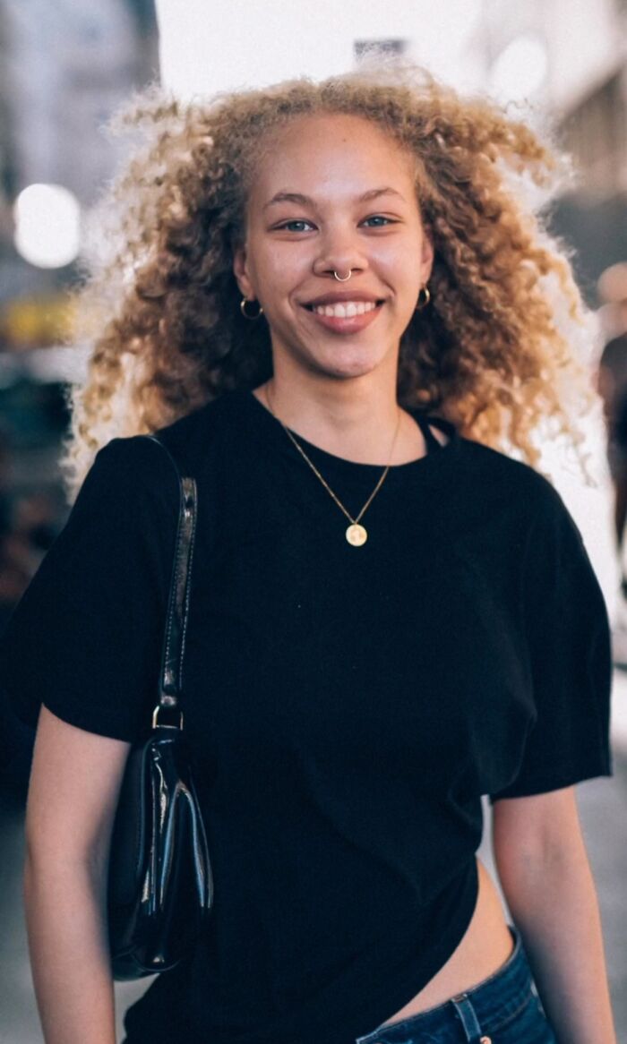 Smiling woman with curly hair in a street portrait, showcasing striking visual style.