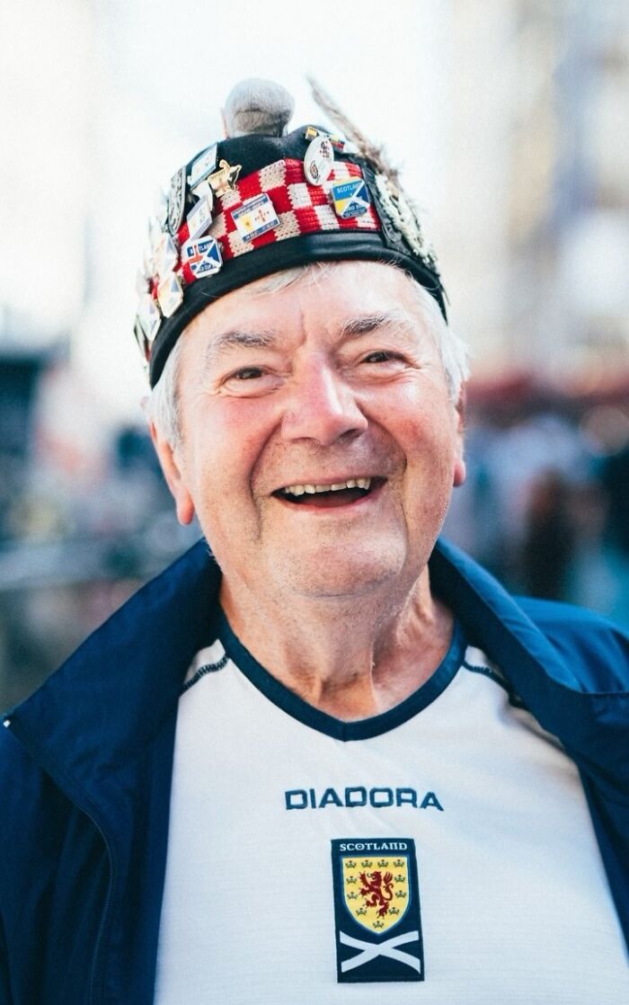 Elderly man smiling, wearing a Scotland hat and shirt; exemplifies visually striking street portraits by the photographer.
