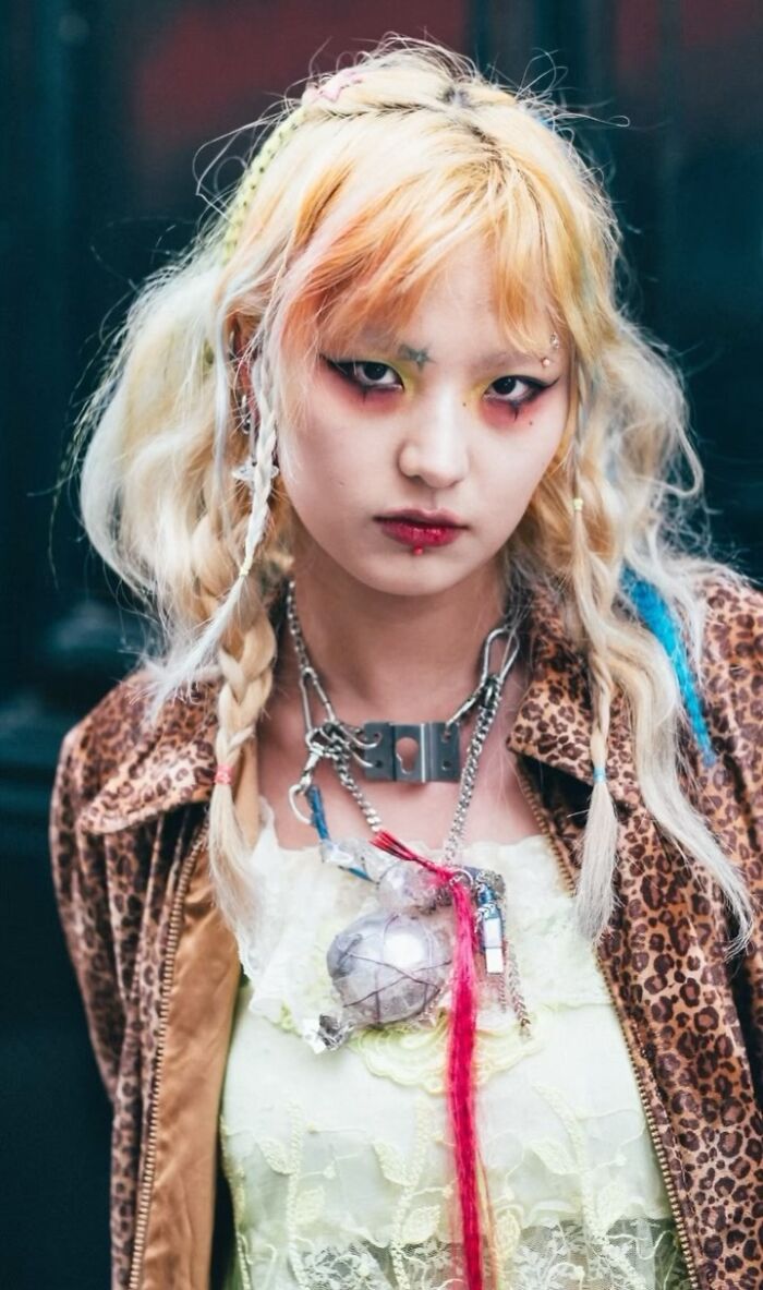 Street portrait of a visually striking individual with vibrant makeup, colorful hair, and eclectic fashion accessories.