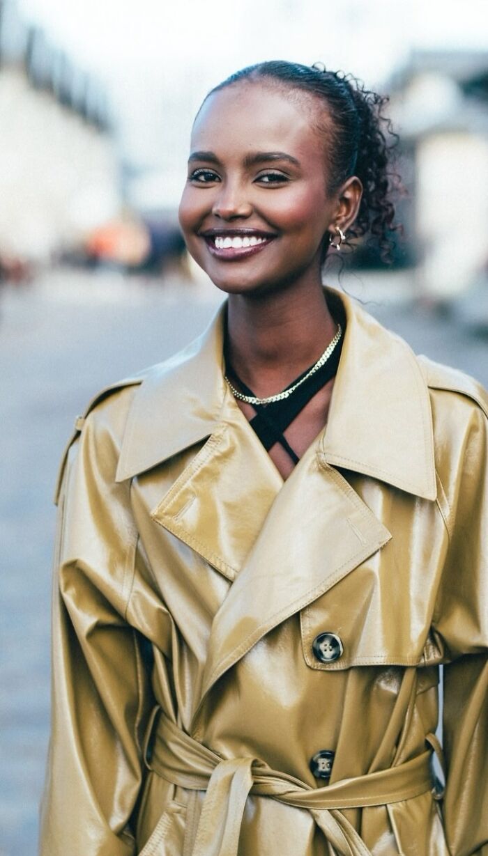 Cheerful woman in a gold trench coat smiling on the street, showcasing striking street portrait photography.
