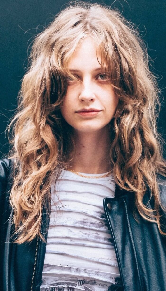 Portrait of a young woman with wavy hair in a black leather jacket, part of a street photography series.