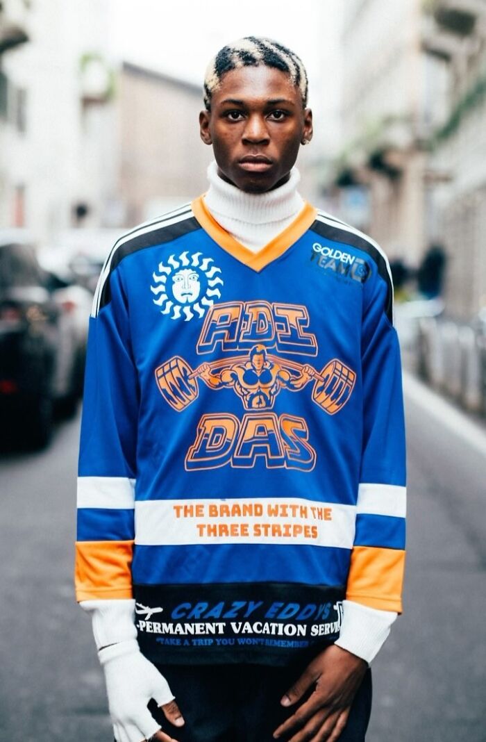 Street portrait of a man in a colorful jersey with graphic designs, standing confidently in an urban setting.