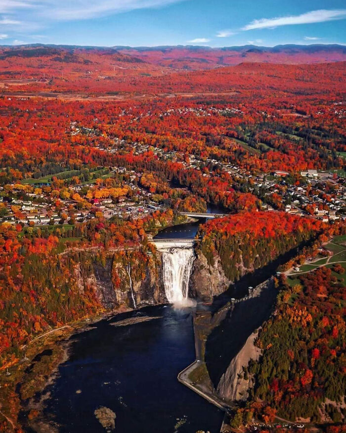 Aerial view of a Canadian waterfall surrounded by vibrant fall foliage and a small town in autumn colors.