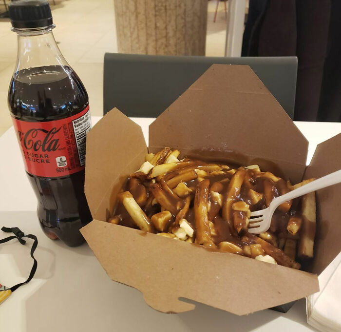 Poutine in a takeout box with a bottle of Coca-Cola, a classic Canadian meal.