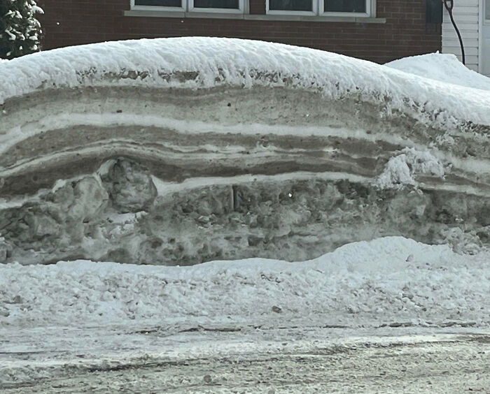 Layered snowbank piled high on a residential street, showing unique winter conditions only happen in Canada.