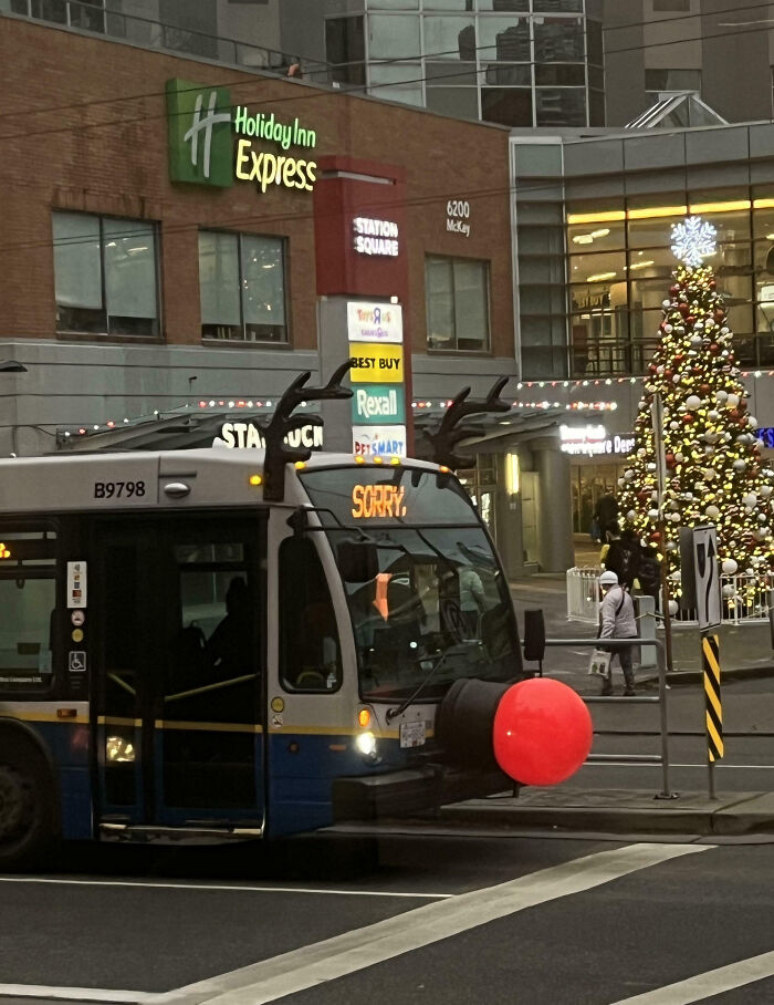 Bus decorated with reindeer antlers and a large red nose driving through a Canadian city during the holiday season