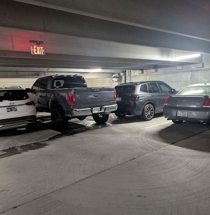 Oversized truck takes up two parking spaces in a crowded garage, highlighting entitled behavior.