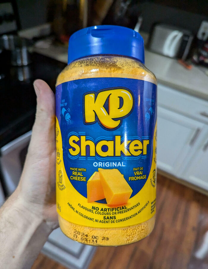 Hand holding a KD Shaker cheese powder jar, representing a classic Canadian snack.