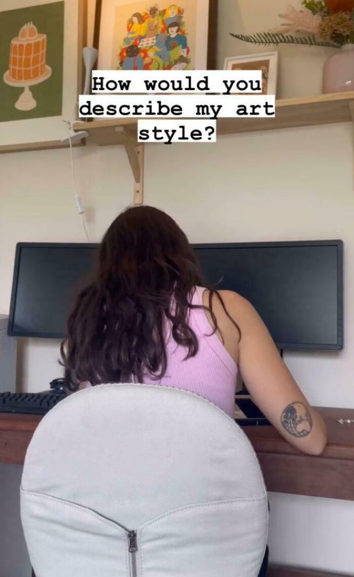 Person at desk with dual monitors, pink top, and tattoo, pondering art style; seriously confusing art-related setup.